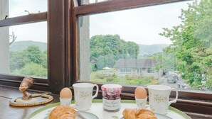 A breakfast setup with croissants, eggs, and jam on a table by a window overlooking a rural landscape. - 3 bedroom accommodation in Bradwell (Bradwell)