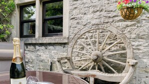 A bottle of champagne and wine glasses on a table with a stone wall and a wooden wheel in the background. - 3 bedroom accommodation in Bradwell (Bradwell)