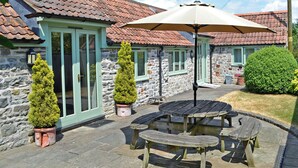 Ein Steinhaus mit Ziegeldach, einer Terrasse mit Holzmöbeln und Blumentöpfen.