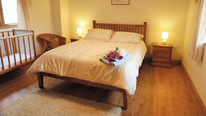 Ein ordentlich eingerichtetes Schlafzimmer mit einem hölzernen Bett, Nachttischen mit Lampen, einem kleinen Stuhl und einem Babybett.