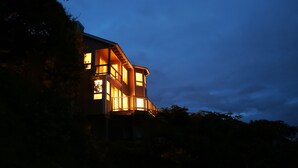A multi-story building with illuminated windows and a balcony, surrounded by trees. - Oceanside View House (Oceanside)