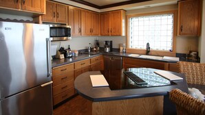 A compact kitchen with wooden cabinets, a stainless steel refrigerator, a microwave, and a coffee maker. - Oceanside View House (Oceanside)