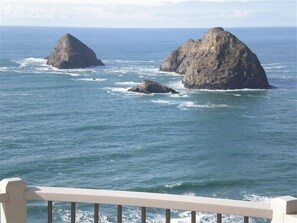 Une vue côtière avec deux formations rocheuses imposantes dans la mer, une rambarde au premier plan et un ciel dégagé.