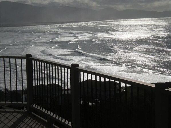 Une vue sur la côte, prise depuis un balcon doté d’une balustrade, avec l’océan et des montagnes lointaines en toile de fond.