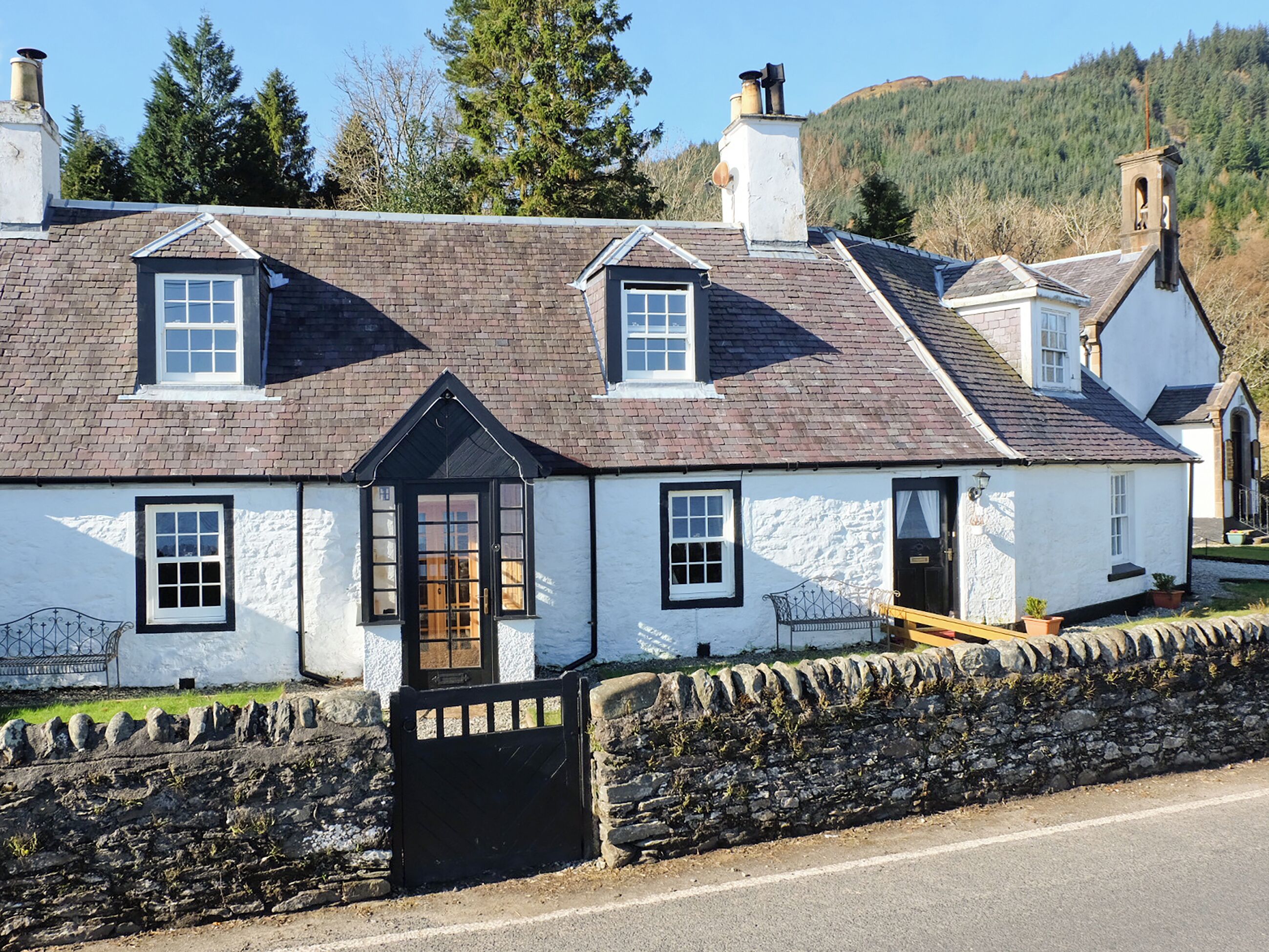 A traditional white building with a black door, multiple windows, and a stone wall in front.