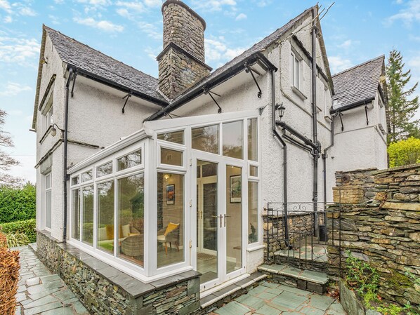 A house with a stone chimney, a conservatory with glass doors, and a stone wall.