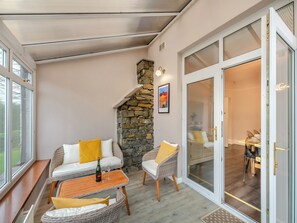 A cozy patio area with wicker furniture, a stone fireplace, and a glass door leading to an interior dining space.