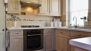 Una cocina con armarios de madera, estufa a gas, horno y una ventana con persianas.