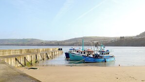 A harbor with boats docked at a concrete pier, surrounded by calm water and distant hills.