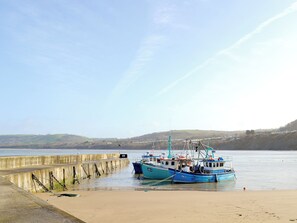 A harbor with boats docked at a concrete pier, surrounded by calm water and distant hills.