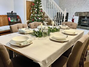A dining table set with white plates and glasses, a Christmas tree, and a candle.