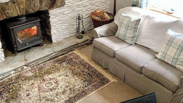 A cozy living room with a stone fireplace, a sofa with plaid cushions, and a patterned rug.