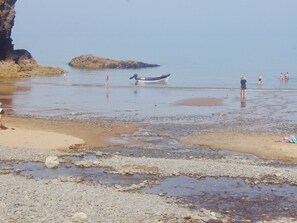 A rocky beach with a boat, people, and a cliff.