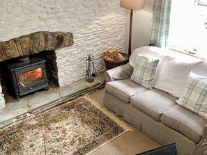 A cozy living room with a stone fireplace, a sofa with plaid cushions, and a patterned rug.