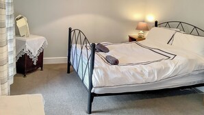 A single bed with a metal frame, a bedside table with a lamp, a mirror, and a small dresser.