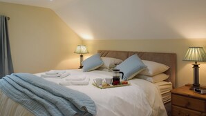 Un letto rifatto con cuscini, un comodino con una lampada e un vassoio con una tazza e una mela.