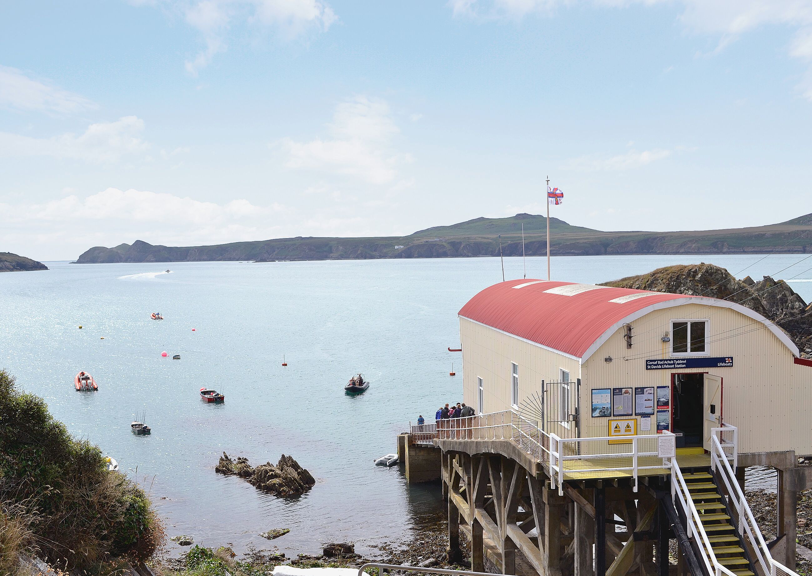 A coastal lifeboat station with a red-roofed building, a pier, and boats in the water.