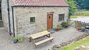 Une maison en pierre avec un toit en tuiles, une porte en bois et un banc à l’extérieur.
