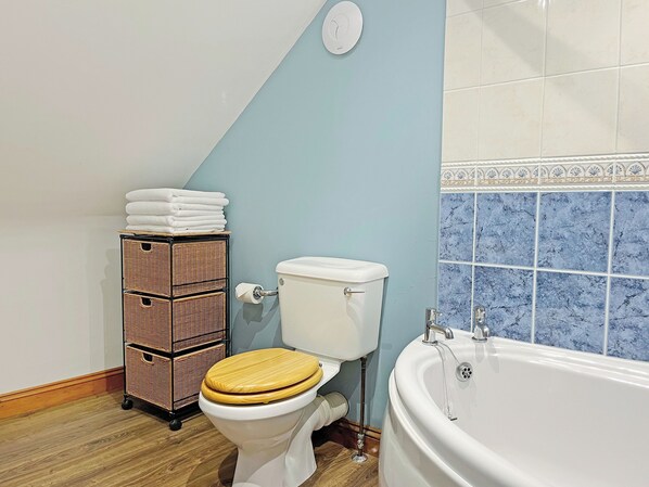 A bathroom with a toilet, a wicker basket with towels, and a bathtub.