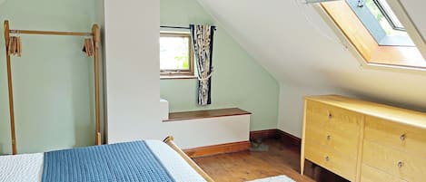 A bedroom with a sloped ceiling, a bed with a blue quilt, a wooden dresser, and a skylight.