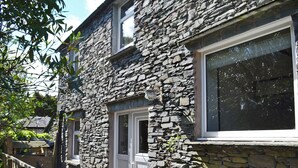 A stone building with a white door, a window, and a small garden area with plants. - 2 bedroom accommodation in Grasmere (Grasmere)