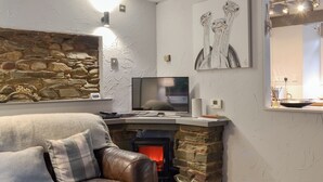 A living room with a stone fireplace, a leather sofa, a flat-screen TV, and wall art. - 2 bedroom accommodation in Grasmere (Grasmere)
