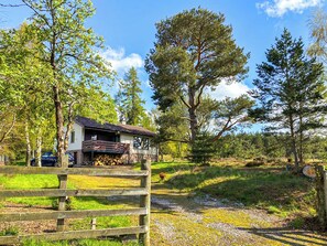 Een rustieke chalet met balkon, omgeven door een houten hek en een grindpad.