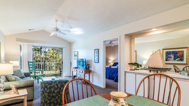 A spacious living area with a dining table, chairs, a sofa, and a balcony with a view of greenery. - TB 9I Super 3rd floor condo True Blue Golf/Tennis Accessible WINTER RENTAL (Pawleys Island)