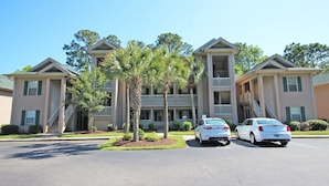 A multi-story building with a central courtyard, featuring a parking area with two cars. - TB 9I Super 3rd floor condo True Blue Golf/Tennis Accessible WINTER RENTAL (Pawleys Island)