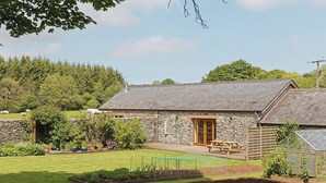 Une ferme en pierre avec une porte en bois, un jardin doté de plates-bandes surélevées et une table de pique-nique.