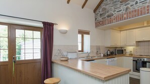 Une cuisine avec un îlot central en bois, des tabourets de bar, un mur d’accent en pierre et une vue par la fenêtre.