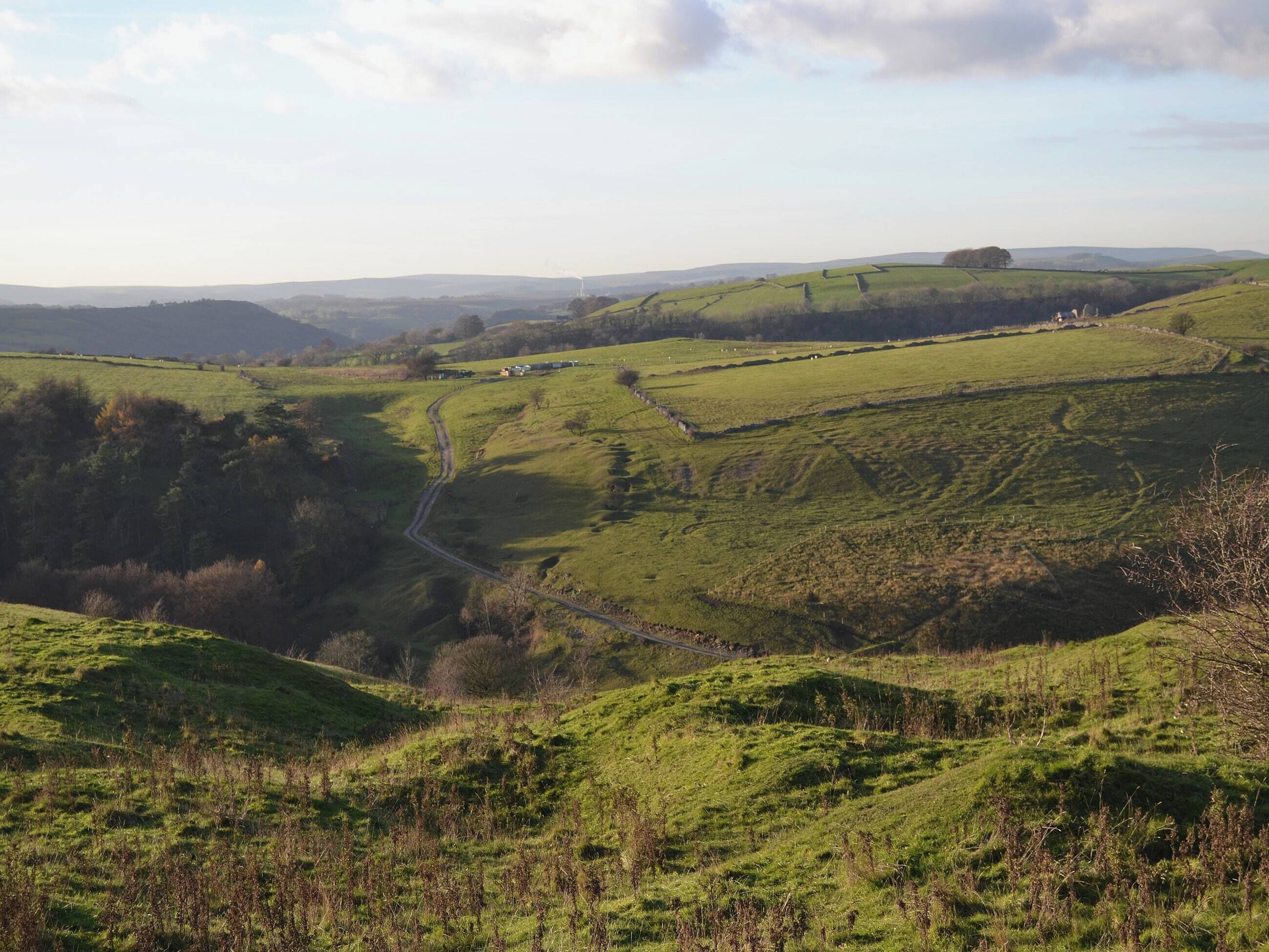 A rural landscape with rolling hills, a winding road, and scattered buildings.