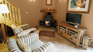 A cozy living room with a fireplace, striped sofas, a television, and a framed picture on the wall.