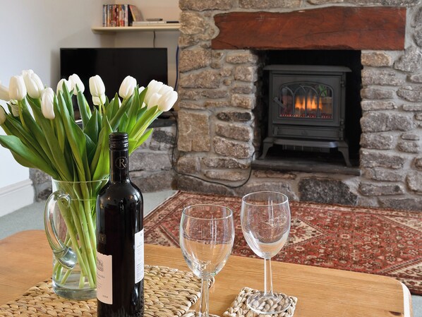 A room with a stone fireplace, a bottle of wine, and two glasses on a wooden table.