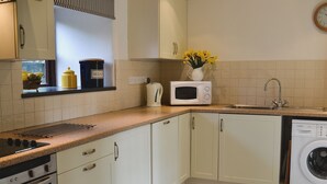 A kitchen with white cabinets, a microwave, a kettle, a sink, and a washing machine. - 2 bedroom accommodation in Altarnun, near Launceston (Altarnun, near Launceston)