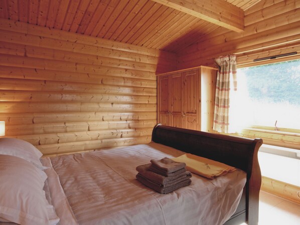 Quarto de cabana de madeira com uma cama, um guarda-roupa e uma janela com cortinas.