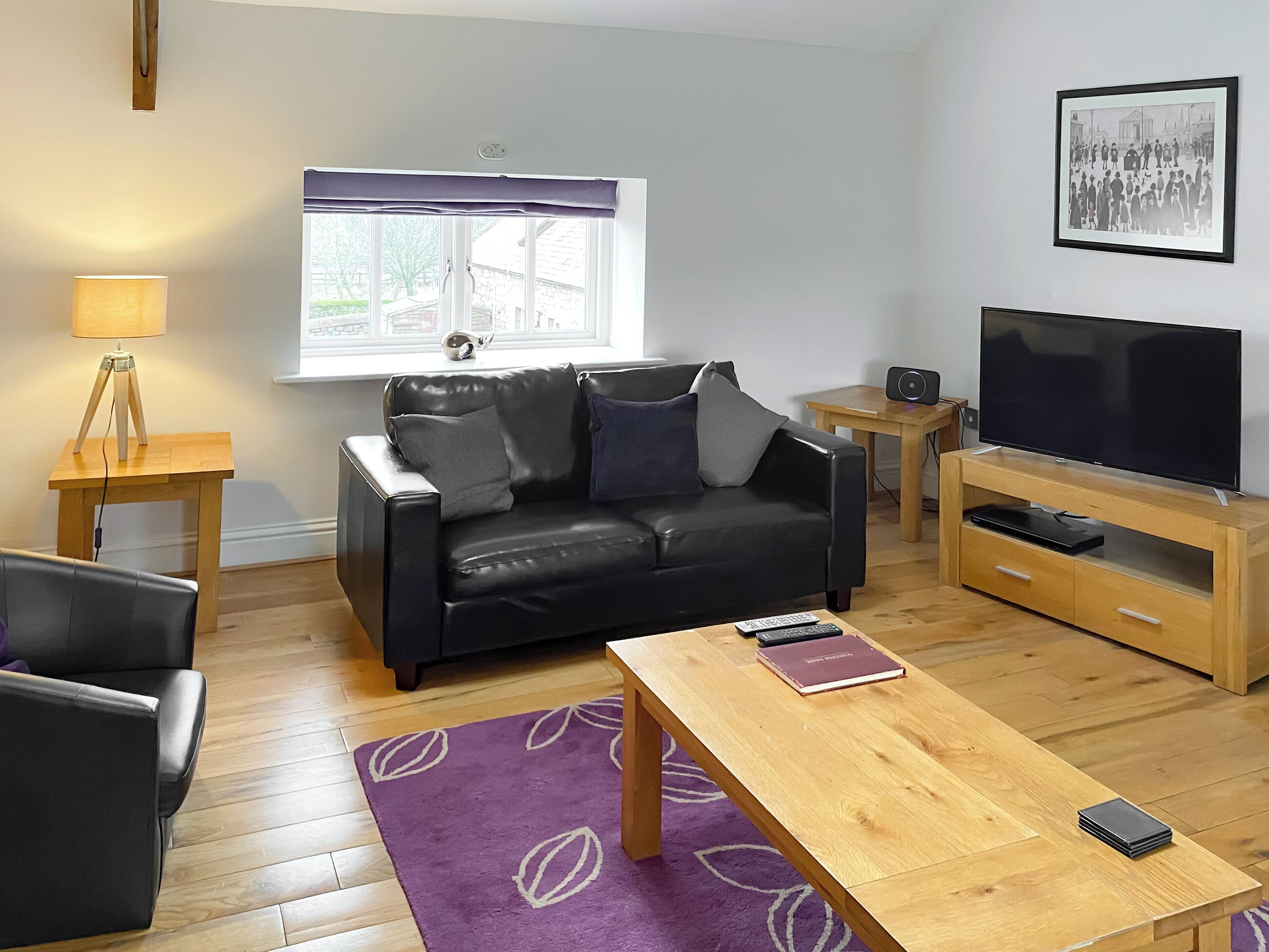 A modern living room with a black leather sofa, a wooden coffee table, a TV on a wooden stand, and a window with a view of the outside.