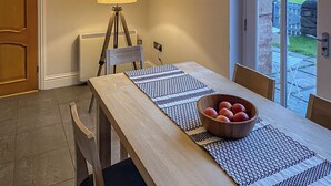 A dining area with a table, chairs, a lamp, a tripod, and a bowl of fruit. - 3 bedroom accommodation in Steading, Berwick-upon-Tweed (Steading, Berwick-upon-Tweed)