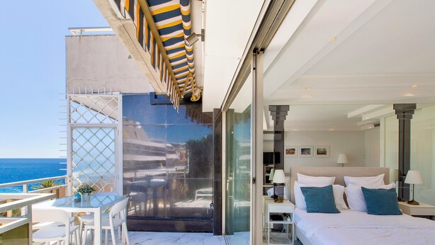 Een moderne slaapkamer met een groot bed, een glazen deur naar een balkon en uitzicht op de zee.