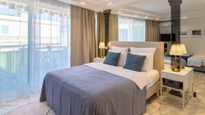 Een moderne hotelkamer met een groot bed, twee nachtkastjes met lampen, een flatscreen televisie en uitzicht op een balkon.