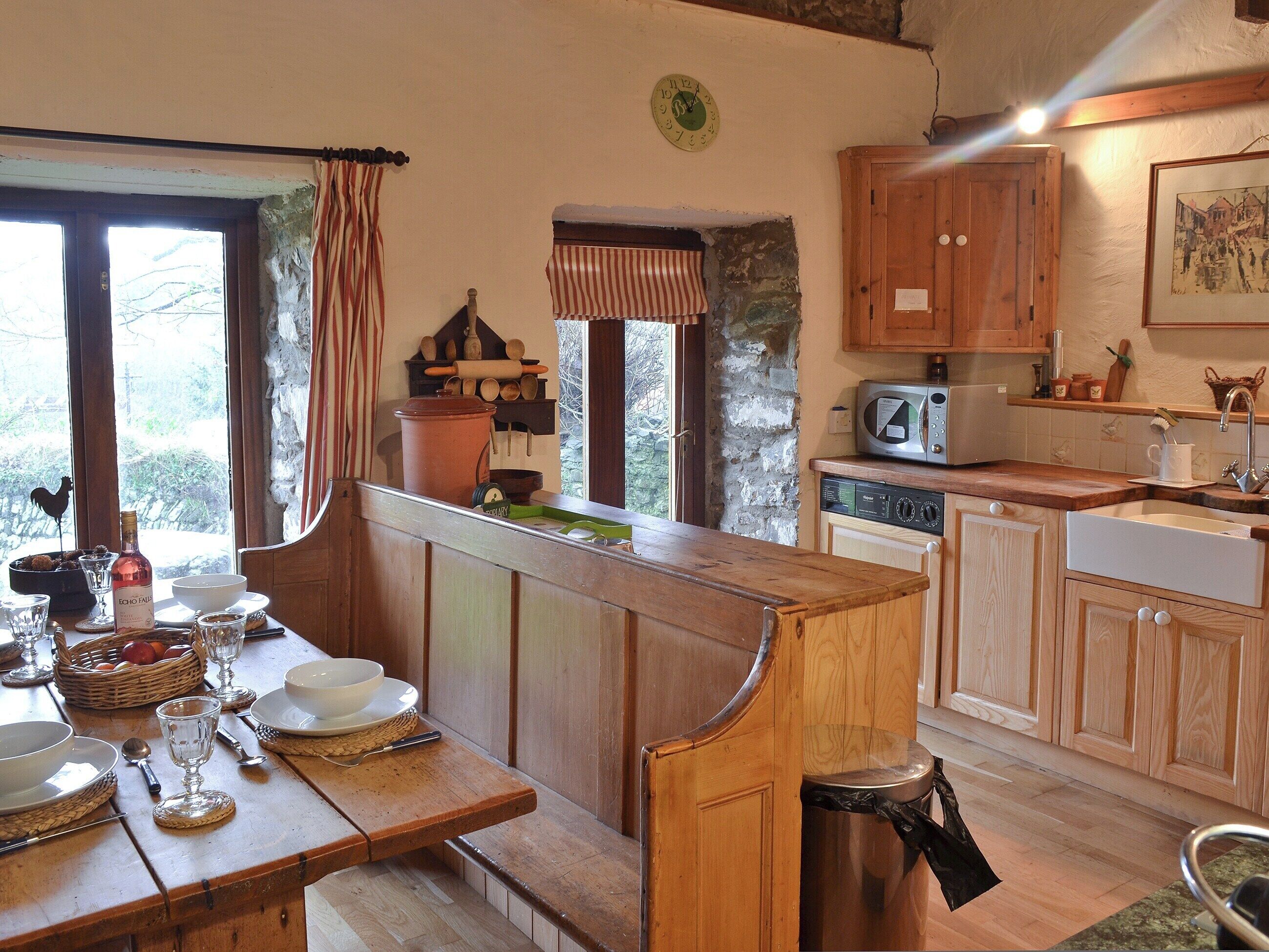A rustic kitchen with wooden cabinetry, a stone wall, and a dining area with a bench.