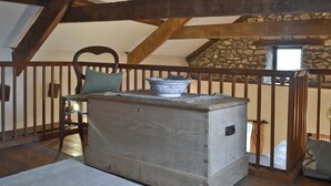 Una stanza rustica con travi a vista in legno, una parete in pietra, una panca di legno con cuscino e una grande ciotola in ceramica su un tavolo di legno.