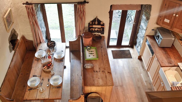 Una cucina rustica con mobili in legno, un tavolo da pranzo apparecchiato per quattro persone e vista sull'esterno attraverso ampie finestre.