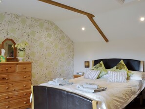 A bedroom with a bed, wooden dresser, floral wallpaper, and a sloped ceiling.