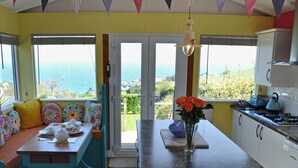 Een keuken met uitzicht op zee, een eethoek met kleurrijke kussens, en een vaas met bloemen op het aanrecht.