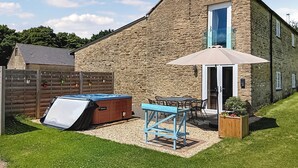 Un edificio de piedra con un patio, un jacuzzi y una mesa con sillas.