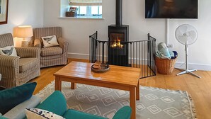 Una sala de estar con chimenea, televisor, sillas a rayas, una mesa y un ventilador.