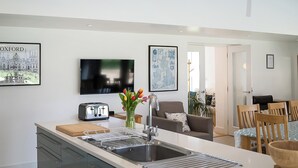 Una cocina moderna con lavavajillas integrado, tostadora y pileta. Hay una zona de comedor con mesa y sillas, y un sofá.