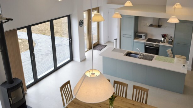 Una cocina moderna con una isla central, un comedor con mesa y sillas de madera, y un ventanal que ofrece vistas al exterior.