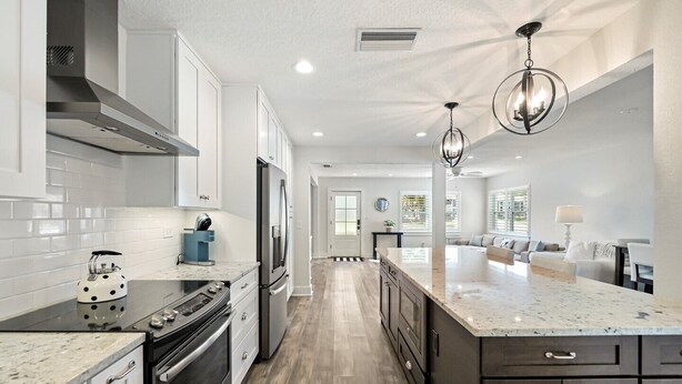 A modern kitchen with white cabinets, a stainless steel refrigerator, a built-in oven, and a large island with a marble countertop. - SaltRunner: Updated 3/2 home with Private Pool (St. Augustine)